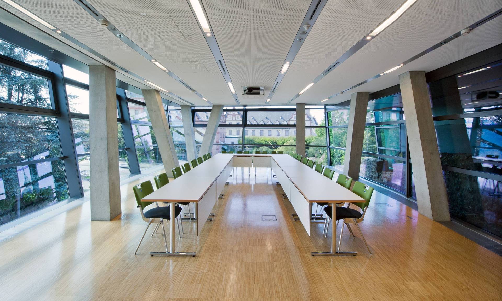 Im lichtdurchfluteten Konferenzraum palladium in der zweiten Ebene ist eine Tischgruppe in U-Form gestellt. Die Tischform ist im Vordergrund offen, im Hintergrund geschlossen. Die Fenster auf der linkem Seite zeigen in Richtung Erich-Ollenhauer-Promenade, die Fenster im Hintergrund in Richtung Schloss.